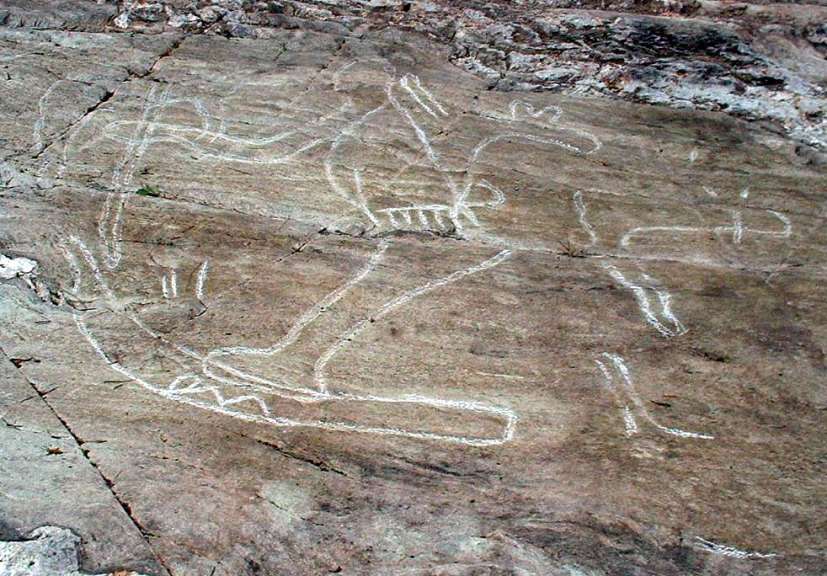 Auf einem Felsen sind weiße Petroglyphen zu sehen, die eine Jagdszene darstellen.