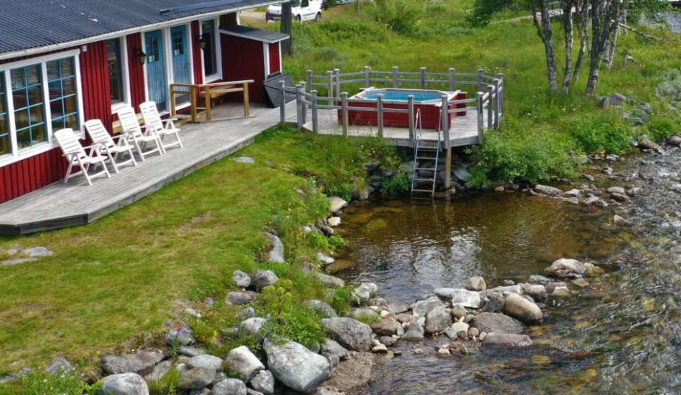 Ein rotes Haus mit einer roten Wanne auf dem Deck neben einem Fluss