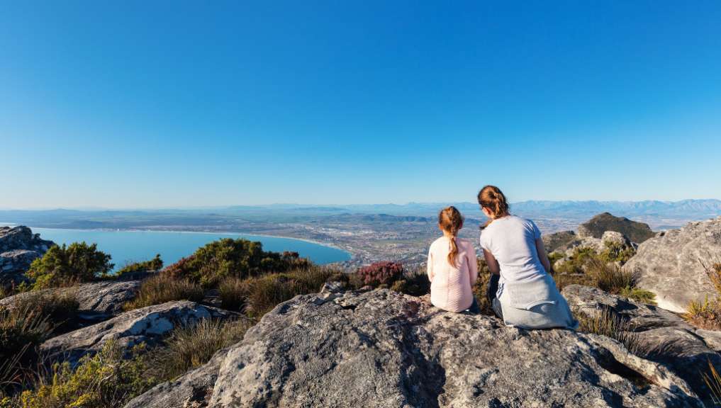 Eine Frau und ein Kind sitzen auf einem Felsen mit Blick auf einen See