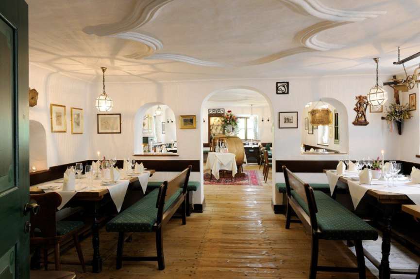 Dieses Bild zeigt das Innere eines eleganten Restaurants mit rustikalen Holzböden, weißen Wänden und gedeckten Tischen.