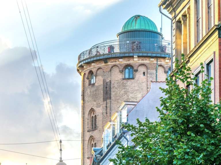 Ein Turm mit einer grünen Kuppel steht zwischen zwei Gebäuden