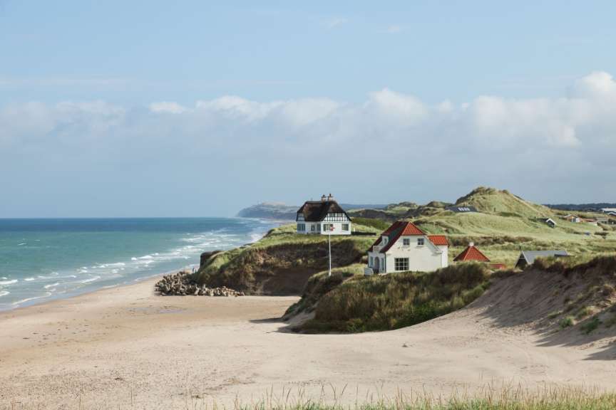 Ein weißes Haus mit einem roten Dach sitzt auf einem Hügel über einem Strand