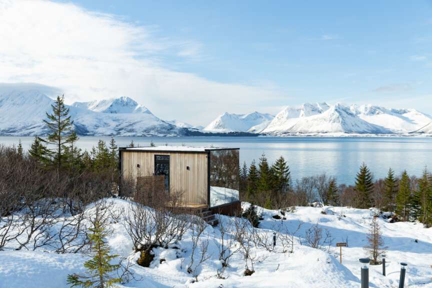 Ein kleines Holzhaus steht inmitten eines schneebedeckten Waldes neben einem See