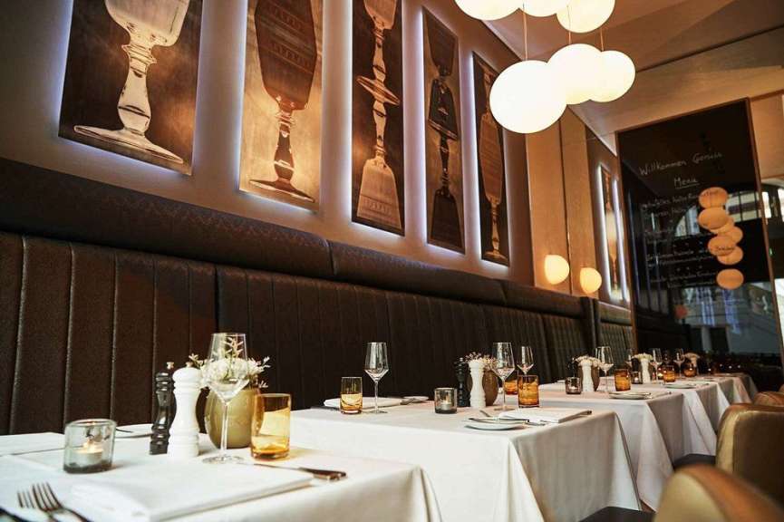 Der Innenraum eines gehobenen Restaurants mit gedeckten Tischen und Kunst an den Wänden ist zu sehen.