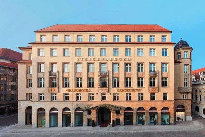 Das Bild zeigt die Fassade eines Hotels, das in hellbeigen Tönen gehalten ist und über ein rotes Dach verfügt.