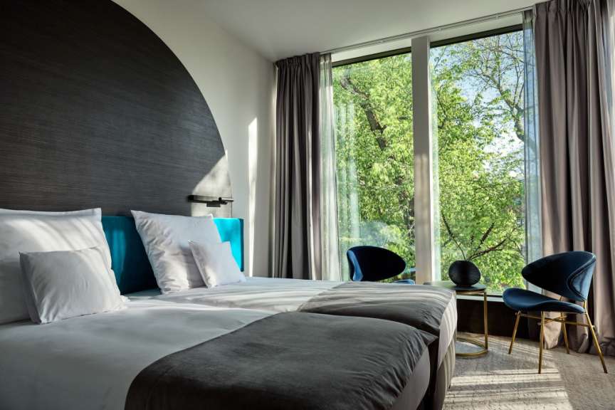 Ein modernes Hotelzimmer mit zwei Betten und einem Fenster, das einen Blick auf grüne Bäume bietet.