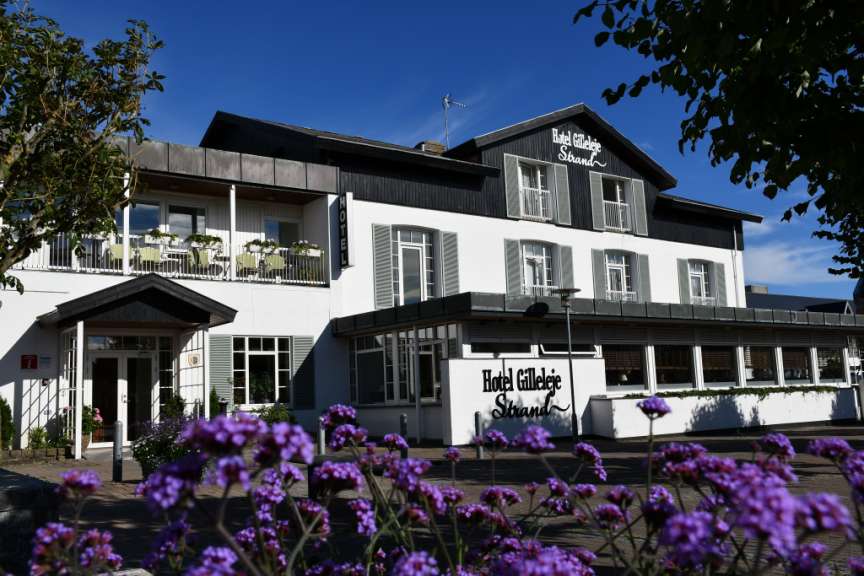 Ein großes weißes Hotel mit lila Blumen vorne