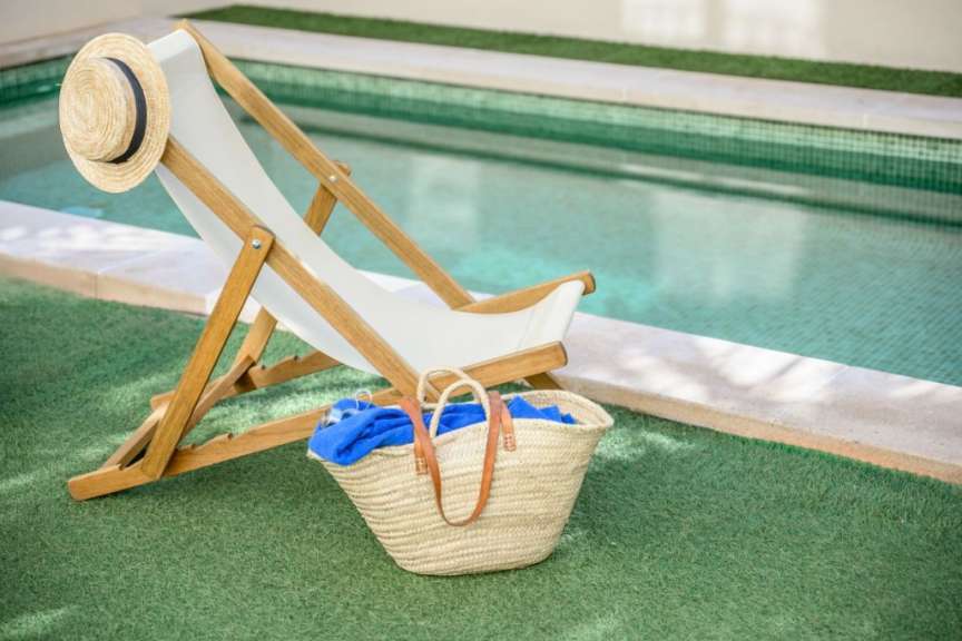 Liegestuhl mit Strohhut und Korb neben einem Pool