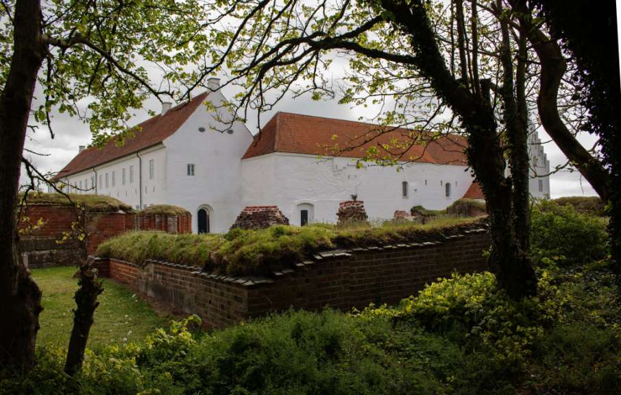Ein weißes Gebäude mit einem roten Dach steht hinter einer Backsteinmauer