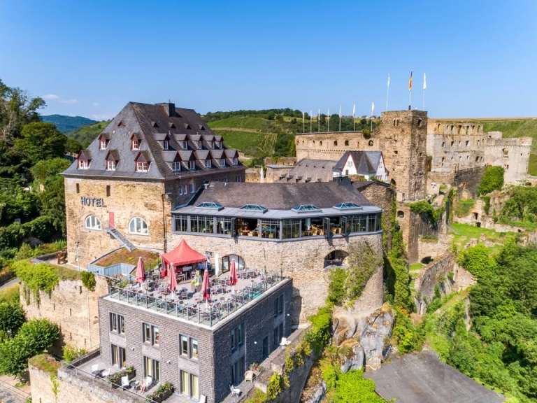Dieses Bild zeigt eine Burg, die teilweise zu einem Hotel umgebaut wurde, mit einer Terrasse und umliegenden Weinbergen.