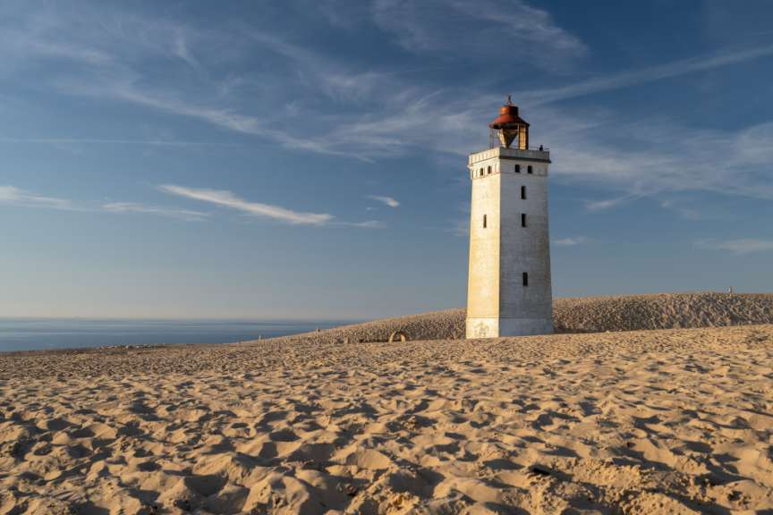 Ein Leuchtturm steht auf einem sandigen Hügel mit Blick auf das Meer