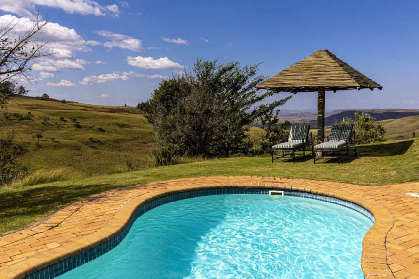 Ein Pool mit Liegestühlen und einem Strohdach im Hintergrund