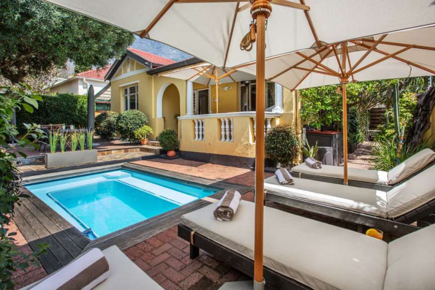 Ein kleiner Pool mit Liegestühlen und Sonnenschirmen vor einem gelben Haus