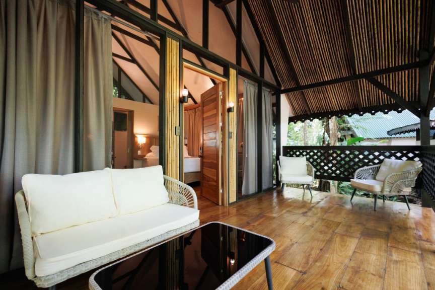 Ein rustikaler Balkon mit zwei Sesseln, einem Sofa, einem Couchtisch und Blick auf ein Schlafzimmer.