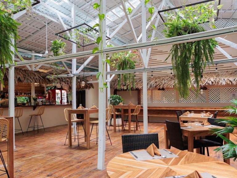 Ein überdachter Innenhof eines Restaurants mit Holzböden, vielen Pflanzen und Strohdächern.