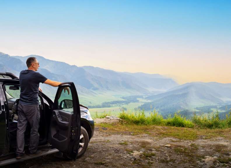 Ein Mann steht neben seinem Auto und schaut auf die Berge