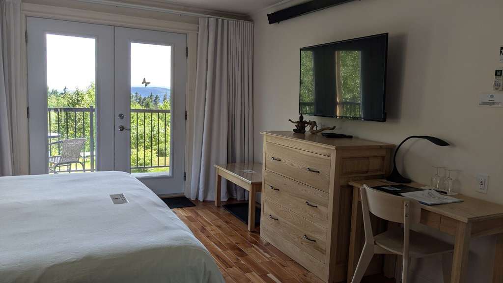 Ein Hotelzimmer mit einem Bett, einem Fernseher, einer Kommode, einem Schreibtisch und einem Balkon mit Blick auf eine grüne Landschaft.