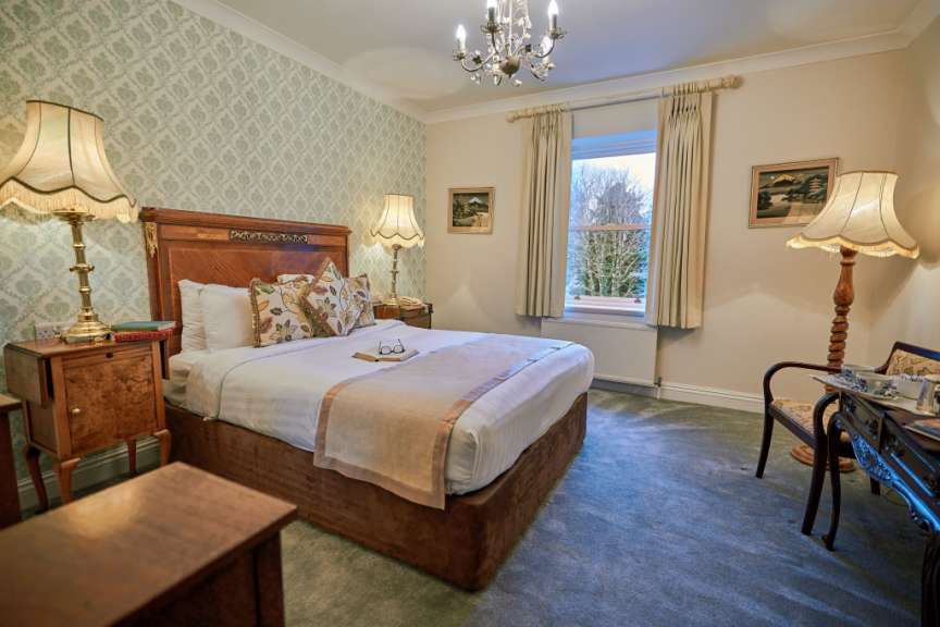 Ein Schlafzimmer ist mit einem Bett, zwei Nachttischen, einem Stuhl und einem Fenster mit Gardinen ausgestattet.