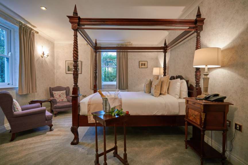 Ein Schlafzimmer mit Himmelbett, zwei Sesseln und einem Champagnerkühler mit Rosen.