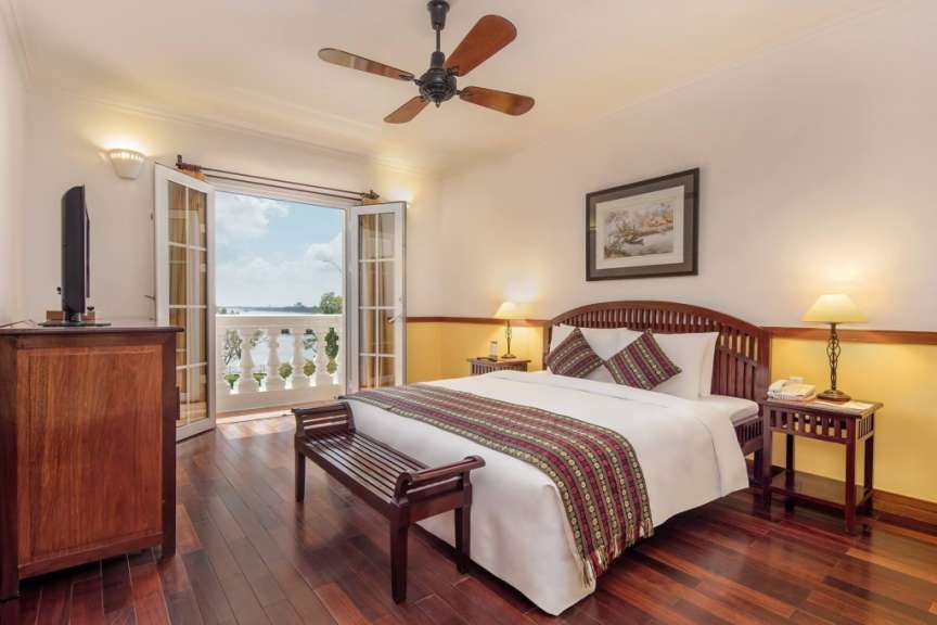 Ein Schlafzimmer mit Doppelbett, zwei Nachttischen, einer Deckenventilator und einer Tür zu einem Balkon.