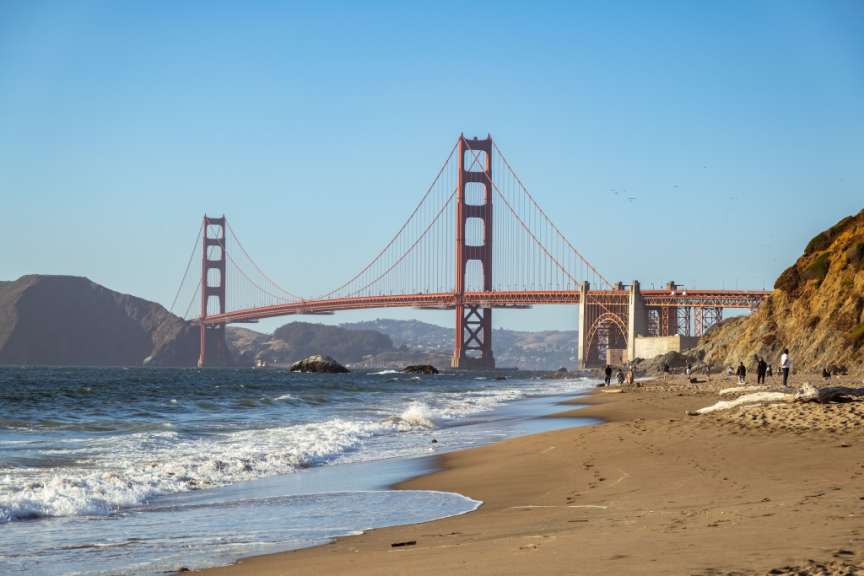 Menschen stehen am Strand vor der goldenen Brücke