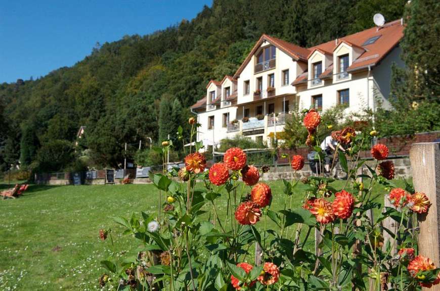 Eine Pension mit roten Dächern und einem umliegenden Garten liegt an einem bewaldeten Hang.
