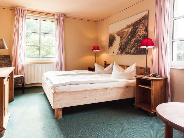 Ein Schlafzimmer mit einem Doppelbett, Nachttischen und einem großen Fenster ist zu sehen.