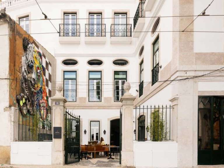 Ein Außenbereich eines Hotels mit einer bunten Wandmalerei, einem Eingangstor und Sitzgelegenheiten.