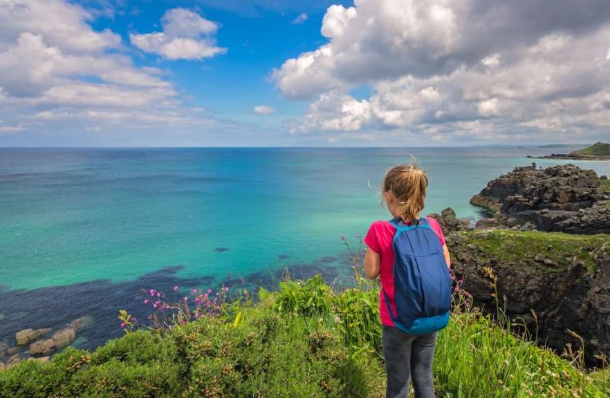 Ein kleines Mädchen mit einem blauen Rucksack schaut auf das Meer