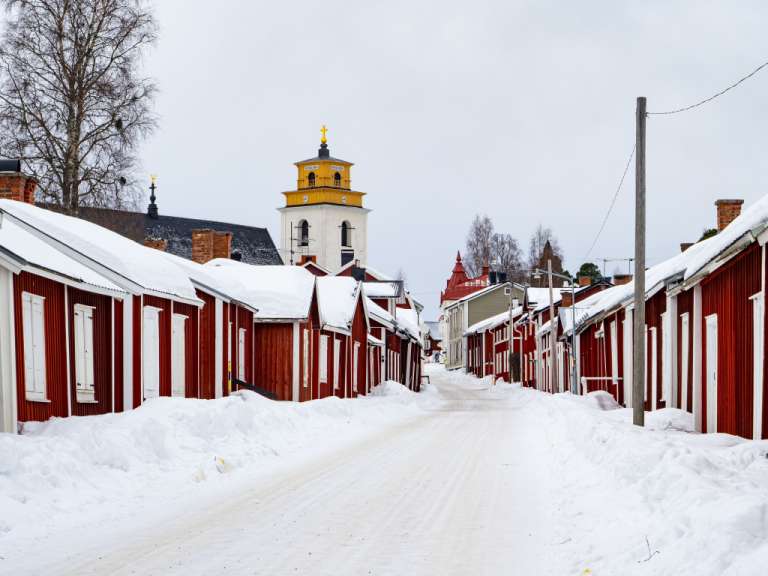 Eine schneebedeckte Straße mit roten Häusern und einer Kirche im Hintergrund