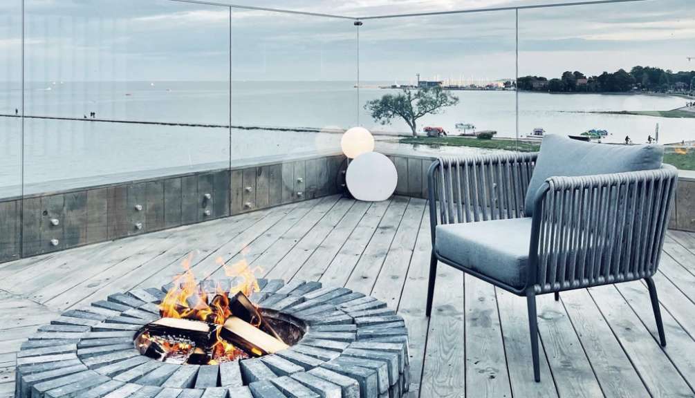 Ein Feuerplatz und ein Stuhl stehen auf einer Holzterrasse mit Blick auf das Meer und eine Stadt.