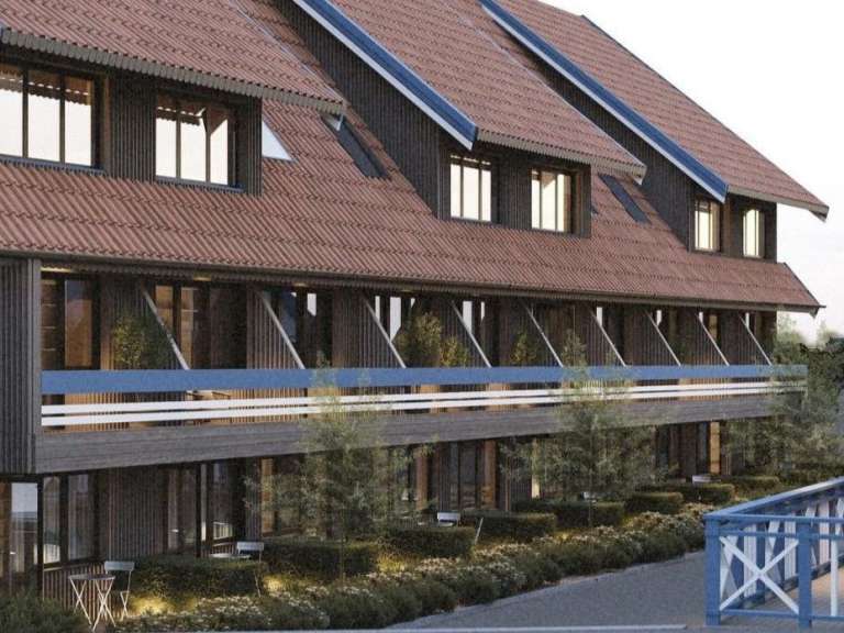 Die Ansicht zeigt die Fassade eines dunklen Holzgebäudes mit mehreren Fensterreihen und einem Balkon, der von einem blauen Geländer gesäumt wird.