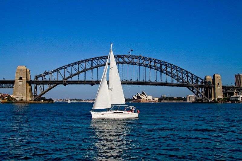 Ein weißes Segelboot schwimmt vor einer Brücke