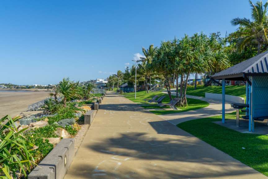 Ein Gehweg an einem Strand mit Bänken und Palmen