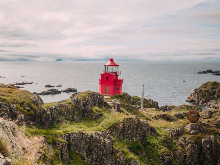 Ein roter Leuchtturm sitzt auf einem felsigen Hügel in der Nähe des Ozeans