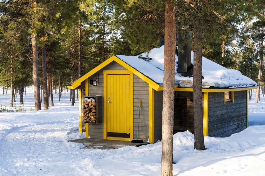 Ein kleines Haus mit einer gelben Tür inmitten eines schneebedeckten Waldes