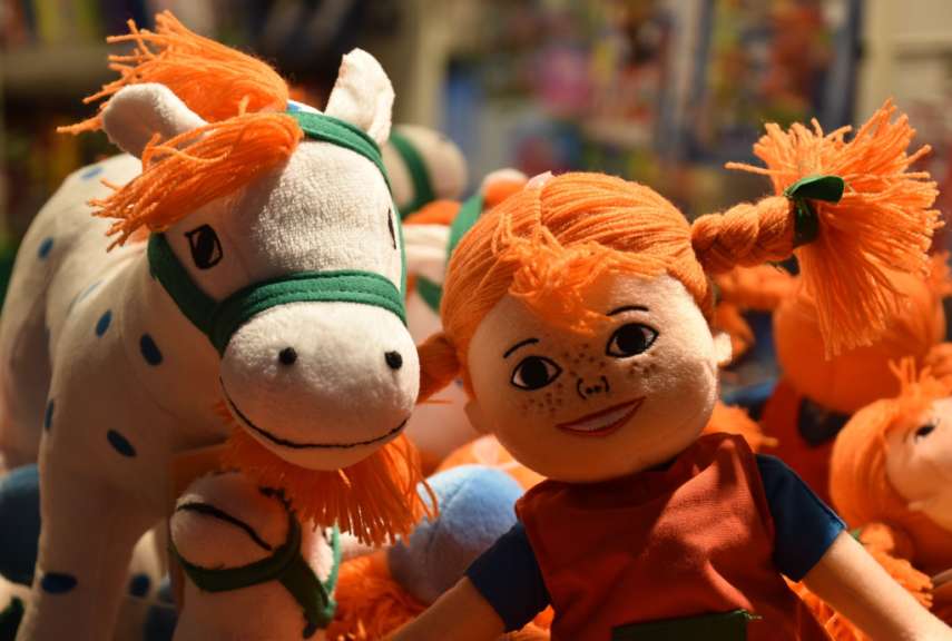 Eine Puppe mit orangefarbenen Zöpfen steht neben einem weißen Pferd
