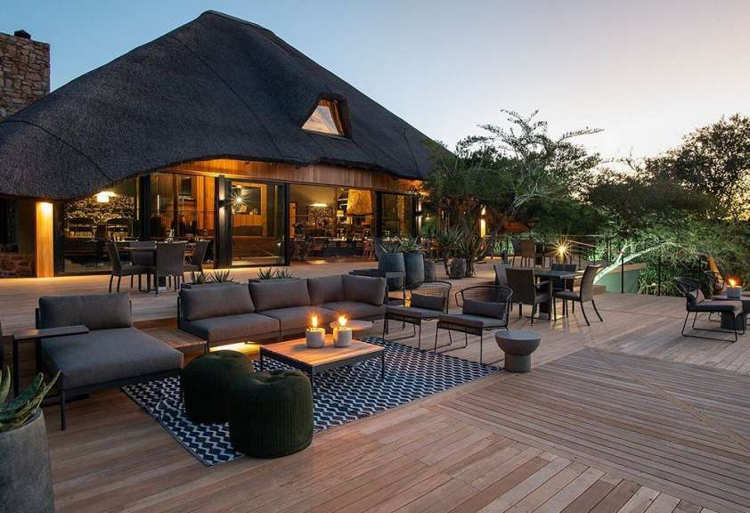 Eine Terrasse mit Möbeln und Kerzen auf einem Holzdeck vor einem Haus mit Strohdach
