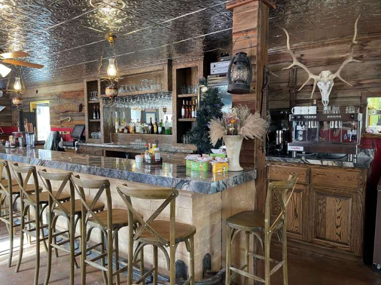 Eine Bar mit Holztresen, Hockern, einem Kaffeeautomaten und einem Geweih an der Holzwand.