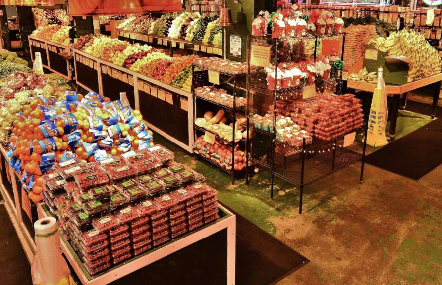 Ein Supermarkt präsentiert seine Obst- und Gemüseauswahl, darunter Berge von Mandarinen und Erdbeeren, die auf mehreren Ebenen ausgelegt sind.