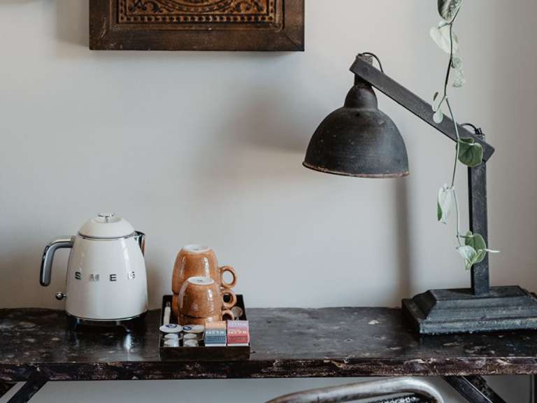 Ein smeg-Wasserkocher steht auf einem Schreibtisch neben einer Lampe und Tassen