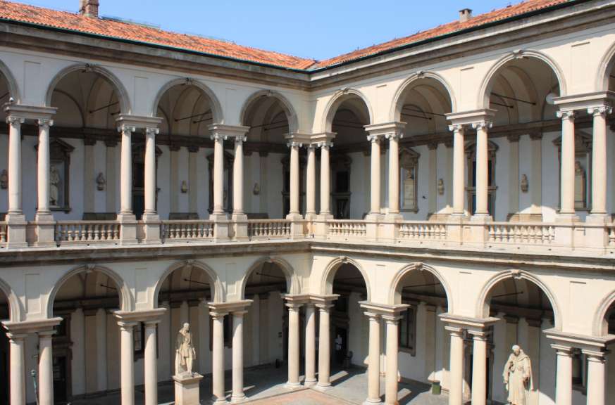 Eine zweistöckige Renaissance-Arkadenhofanlage mit Säulen und Bögen ist unter einem blauen Himmel zu sehen.