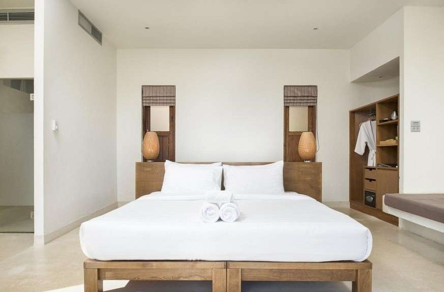 Ein großes weißes Bett mit Holzbettrahmen und zwei Nachttischlampen steht in einem minimalistisch eingerichteten Schlafzimmer.