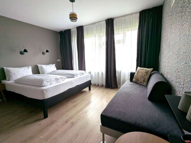 Ein Hotelzimmer mit zwei Betten, einem Sofa und einer floralen Tapete ist im Bild zu sehen.