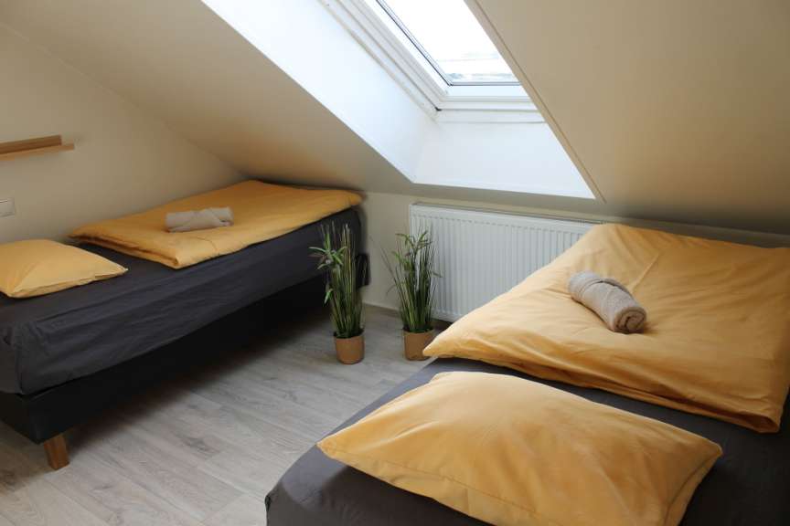 Das Bild zeigt ein Schlafzimmer mit zwei Betten, die mit gelben Laken bezogen sind, einer Dachschräge und einem Dachfenster.