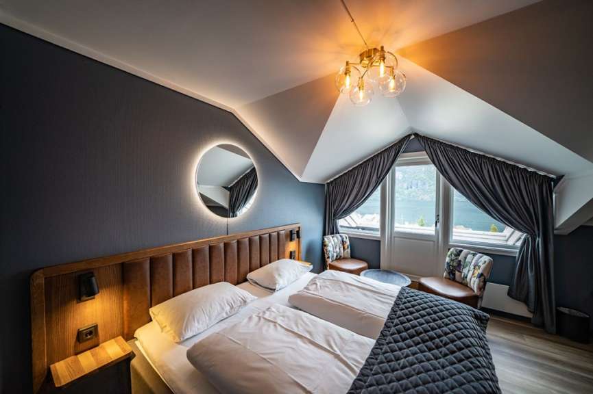 Ein modern eingerichtetes Schlafzimmer mit Doppelbett, Sesseln und einem Ausblick auf eine fjordähnliche Landschaft.