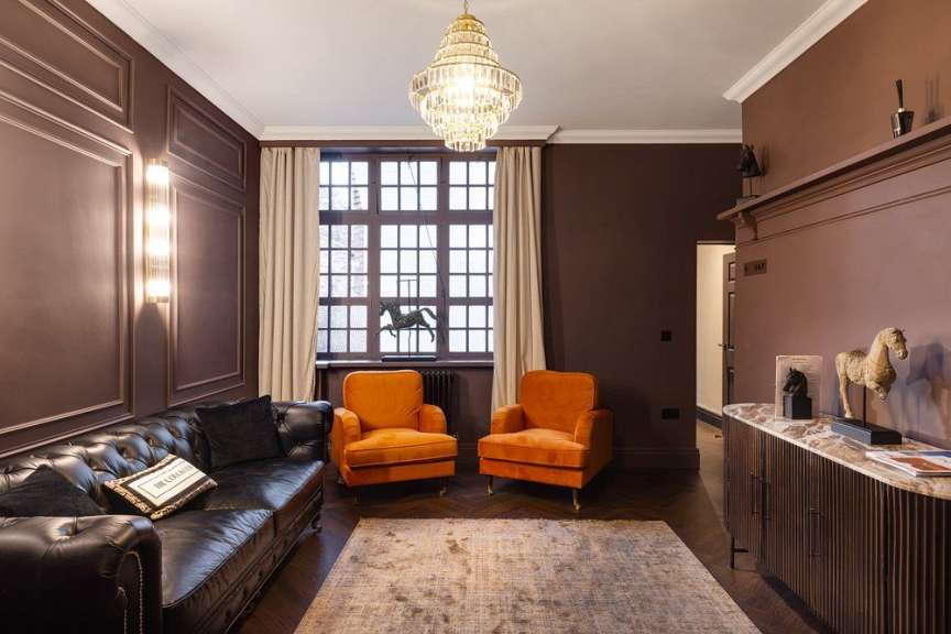 Ein Wohnzimmer mit einem schwarzen Ledersofa, zwei orangefarbenen Sesseln, einem Holzboden, einem Teppich und einer Statue eines Pferdes.