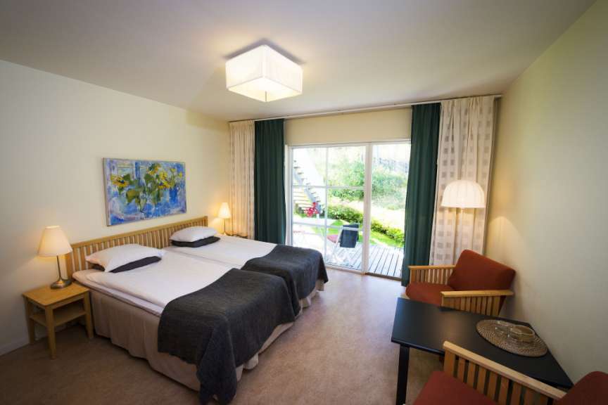 Ein Hotelzimmer mit zwei Betten, einem Gemälde, zwei Sesseln und einem Tisch mit Blick auf eine Terrasse.