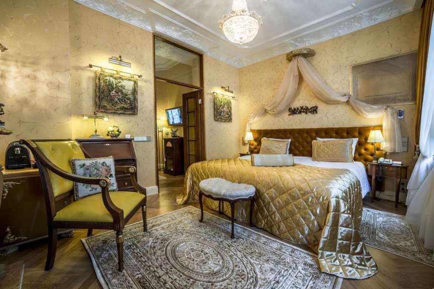 Dieses Bild zeigt ein opulent eingerichtetes Schlafzimmer mit einem großen, goldenen Bett, einem gelben Sessel und antiken Möbeln.