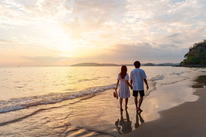 Ein Liebespaar spaziert Hand in Hand am Strand entlang, während die Sonne untergeht.